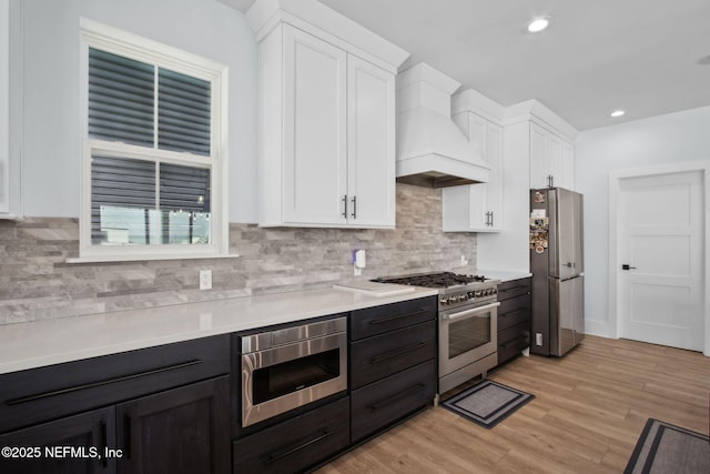 548 Sea Island Dr, Fernandina Beach, FL 32034 - kitchen featuring stainless steel appliances, custom range hood, white cabinets, light countertops, and decorative backsplash
