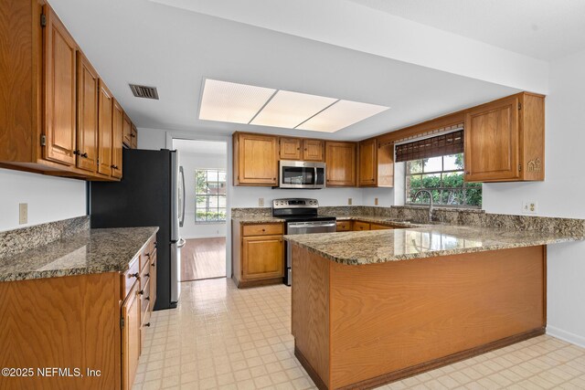 1228 Old Mill Rd, Orlando, FL 32806 - kitchen featuring visible vents, brown cabinetry, a peninsula, a sink, and stainless steel appliances