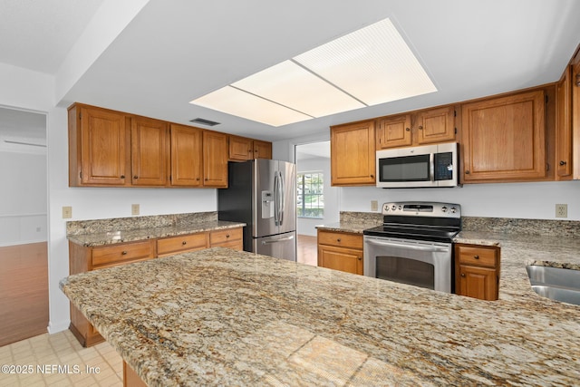 1228 Old Mill Rd, Orlando, FL 32806 - kitchen with visible vents, brown cabinetry, appliances with stainless steel finishes, and a peninsula