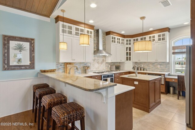 111 Cherry St, Neptune Beach, FL 32266 - kitchen with stainless steel appliances, a peninsula, a sink, visible vents, and wall chimney range hood