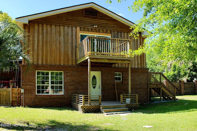 back of property with fence, brick siding, a lawn, a balcony, and board and batten siding