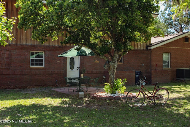 back of house featuring brick siding, a yard, cooling unit, and a patio