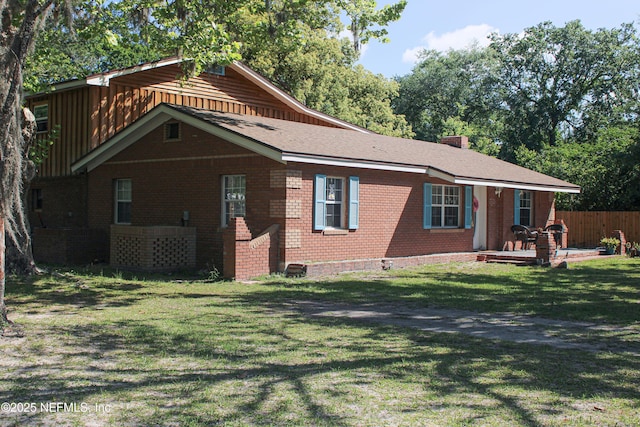 rear view of property featuring a chimney, brick siding, fence, and a yard