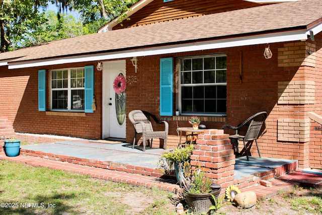 back of house with brick siding and roof with shingles