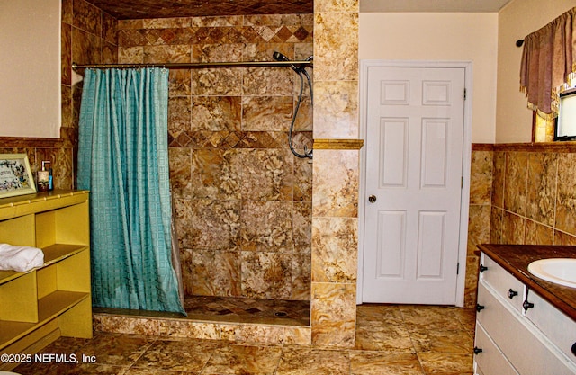bathroom with wainscoting, a tile shower, vanity, and tile walls