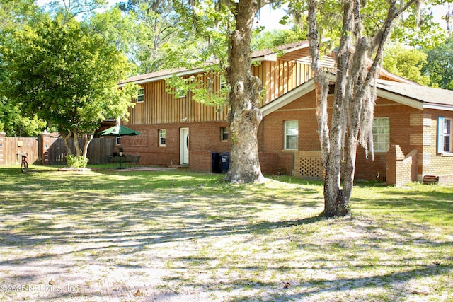rear view of property featuring brick siding, a yard, and fence