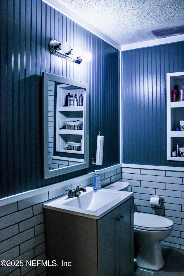 bathroom with toilet, vanity, a textured ceiling, and a wainscoted wall
