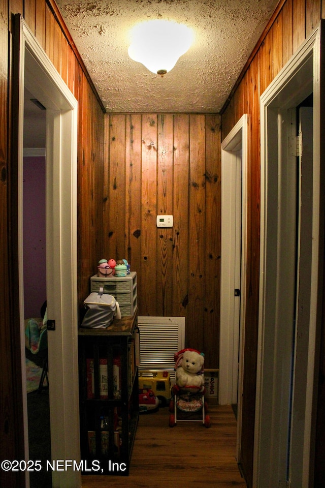 hall with wood walls, wood finished floors, and a textured ceiling