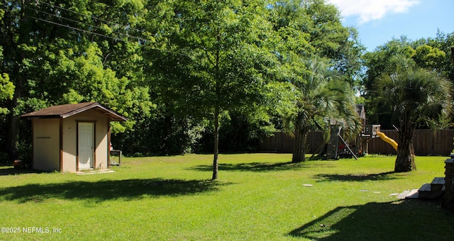 view of yard with fence, a storage unit, an outbuilding, and a playground
