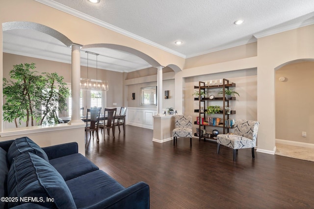 living area with arched walkways, dark wood finished floors, a textured ceiling, and ornate columns