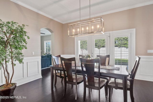 dining room featuring wainscoting, arched walkways, dark wood-type flooring, and ornamental molding