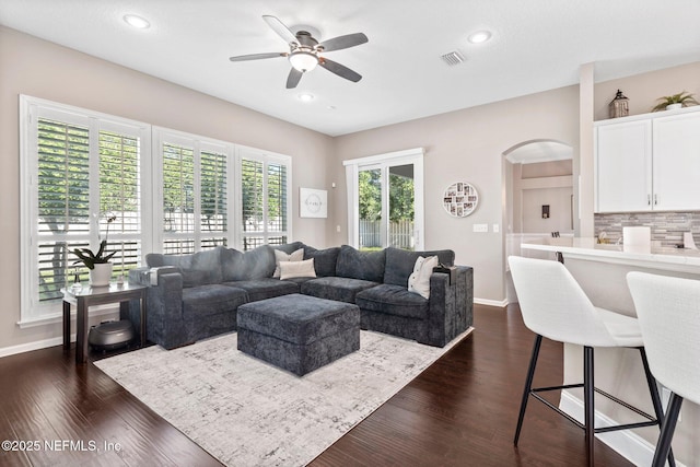 living area with baseboards, visible vents, arched walkways, and ceiling fan