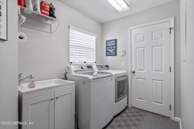 washroom with tile patterned floors, a sink, washing machine and dryer, cabinet space, and a textured ceiling