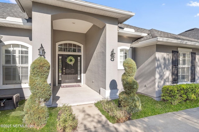 view of exterior entry featuring a shingled roof and stucco siding