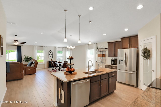 kitchen featuring a sink, hanging light fixtures, light wood finished floors, appliances with stainless steel finishes, and light stone countertops