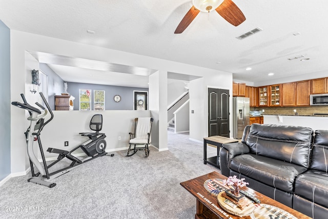 living area with visible vents, a ceiling fan, stairs, baseboards, and light colored carpet