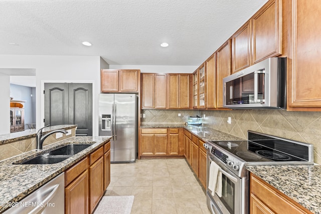 kitchen featuring brown cabinets, appliances with stainless steel finishes, a sink, and stone counters