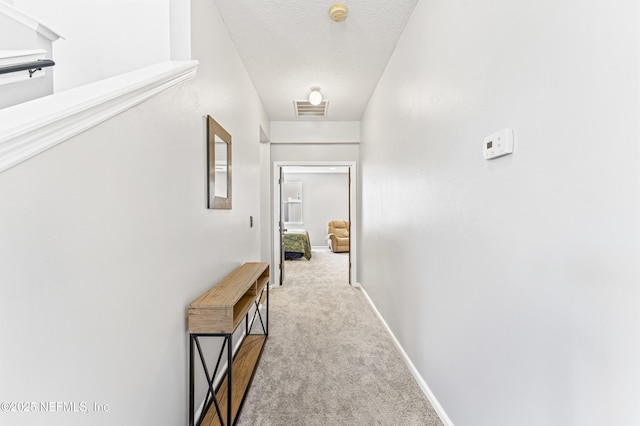 corridor featuring a textured ceiling, carpet floors, visible vents, and baseboards