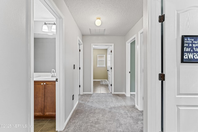 hallway featuring a sink, light tile patterned floors, light colored carpet, baseboards, and visible vents