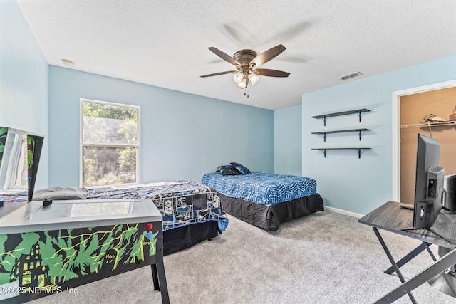 bedroom featuring carpet flooring, a textured ceiling, visible vents, a spacious closet, and ceiling fan