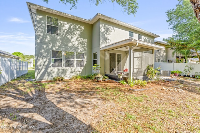 rear view of property featuring stucco siding, a sunroom, and fence