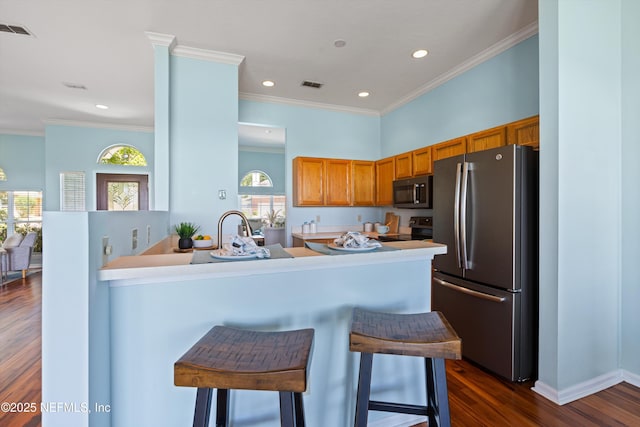 kitchen with visible vents, freestanding refrigerator, brown cabinetry, and a kitchen bar