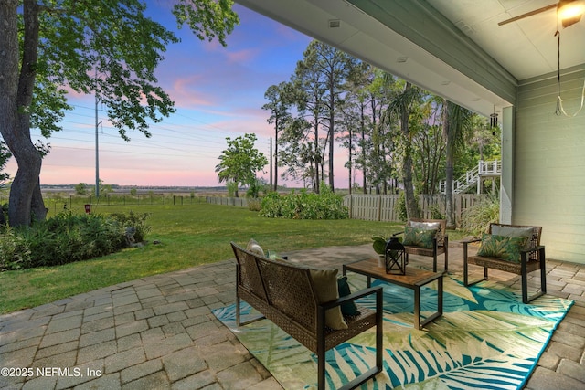 patio terrace at dusk with fence, a ceiling fan, an outdoor hangout area, and a yard