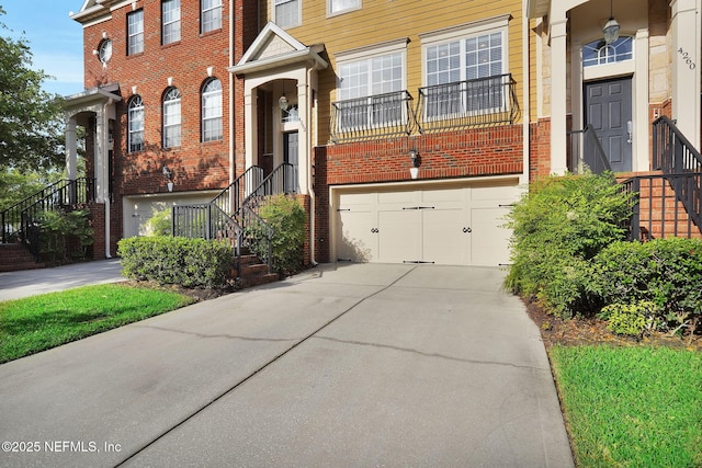 multi unit property featuring brick siding, an attached garage, stairs, and driveway