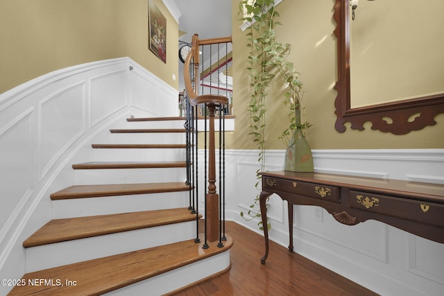 staircase featuring a wainscoted wall, wood finished floors, and a decorative wall