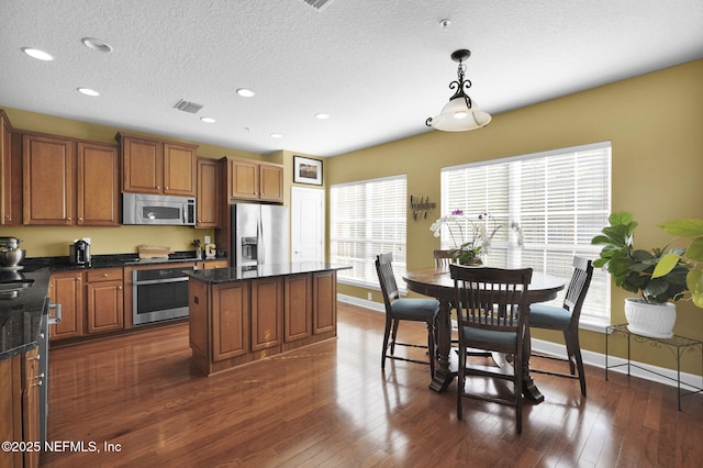 kitchen with brown cabinets, stainless steel appliances, baseboards, visible vents, and a kitchen island