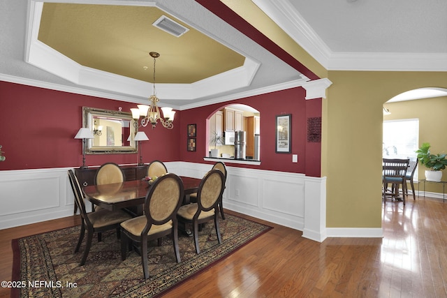 dining space featuring crown molding, hardwood / wood-style flooring, arched walkways, a tray ceiling, and visible vents