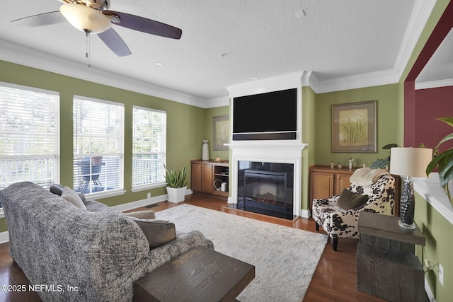 living room featuring a fireplace with flush hearth, dark wood-style flooring, crown molding, and ceiling fan