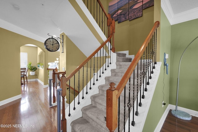 staircase with arched walkways, wood finished floors, crown molding, and baseboards