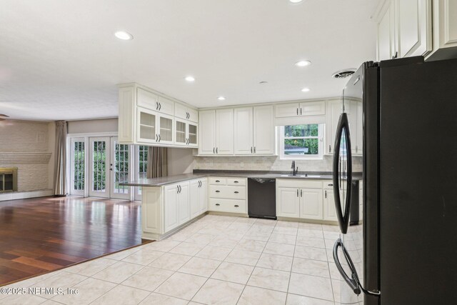 kitchen with a peninsula, open floor plan, tasteful backsplash, glass insert cabinets, and black appliances