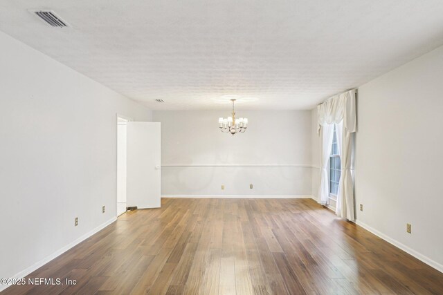 unfurnished room with a chandelier, baseboards, visible vents, and wood finished floors