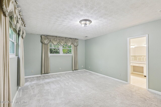 unfurnished bedroom with baseboards, carpet flooring, a textured ceiling, and ensuite bath