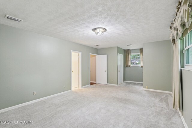 empty room with visible vents, a textured ceiling, baseboards, and carpet floors