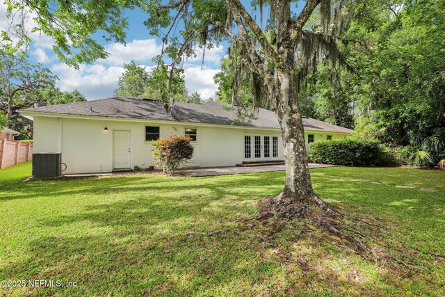 back of property featuring french doors, central AC unit, stucco siding, and a lawn