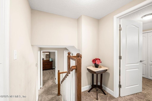 hall with baseboards, carpet flooring, a textured ceiling, and an upstairs landing