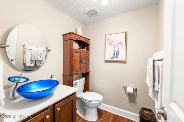 half bath featuring visible vents, wood finished floors, vanity, baseboards, and toilet