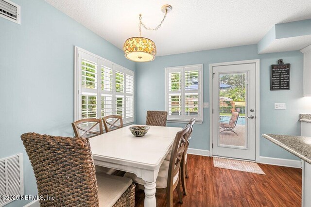 dining space with a textured ceiling, baseboards, visible vents, and dark wood-type flooring