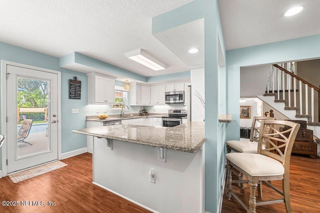kitchen featuring dark wood finished floors, appliances with stainless steel finishes, white cabinets, and a kitchen breakfast bar