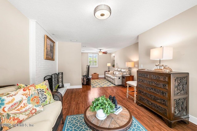living area featuring baseboards, a textured ceiling, ceiling fan, and wood finished floors