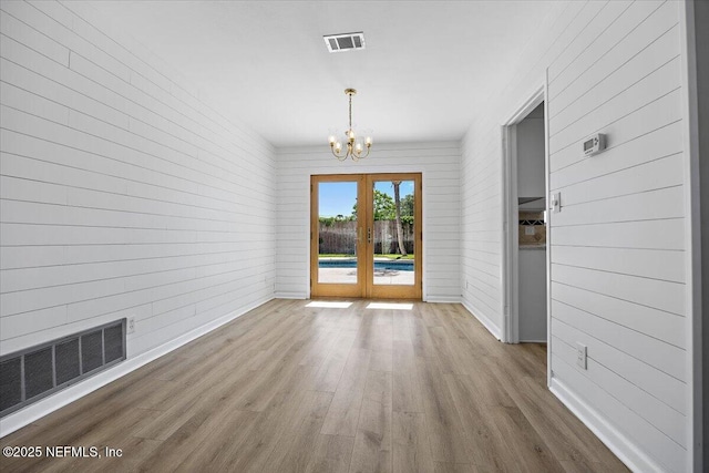 unfurnished dining area featuring visible vents, wood finished floors, a notable chandelier, and french doors