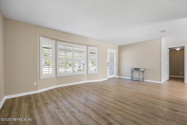 unfurnished living room featuring visible vents, baseboards, and wood finished floors