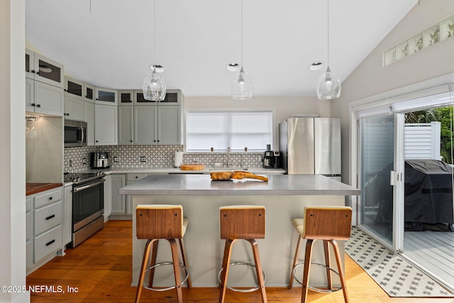 2740 Loja St, Saint Augustine, FL 32084 - kitchen with stainless steel appliances, decorative backsplash, glass insert cabinets, a breakfast bar area, and vaulted ceiling