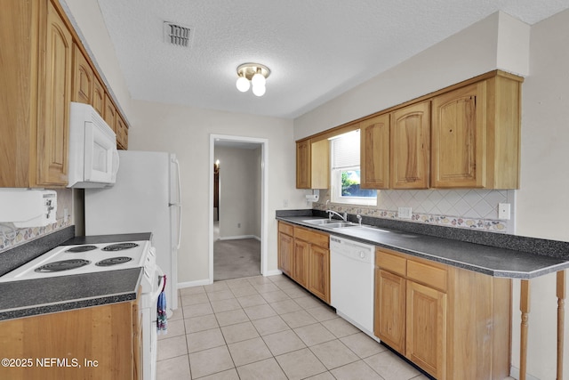 kitchen featuring dark countertops, visible vents, a sink, white appliances, and baseboards