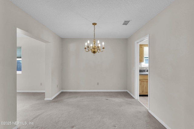 unfurnished room with a textured ceiling, a chandelier, light carpet, baseboards, and visible vents