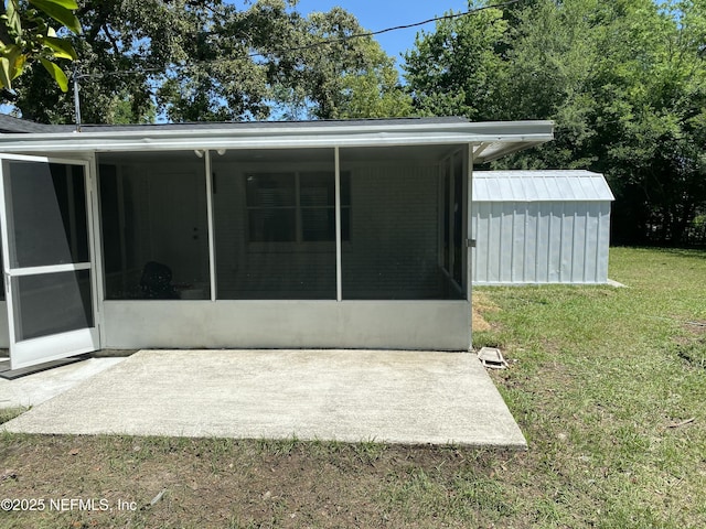 rear view of house with a lawn, an outdoor structure, a sunroom, and a patio