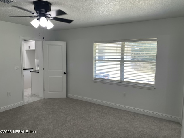 spare room with a textured ceiling, a ceiling fan, baseboards, and light colored carpet